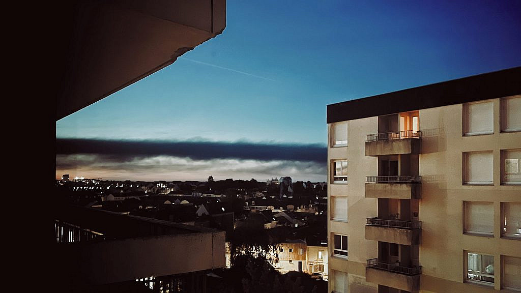 Vue sur la ville vue d'une fenêtre le soir avec des nuages en fond de scène